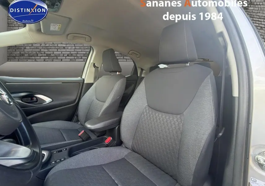 Vue intérieure côté avant droit de la Toyota Yaris Hybrid 2023 avec sellerie tissu gris et accoudoir central.