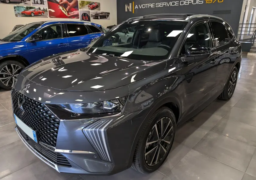 DS7 BlueHDi 130 gris en 3/4 avant droit, avec calandre distinctive et jantes bi-ton en showroom.