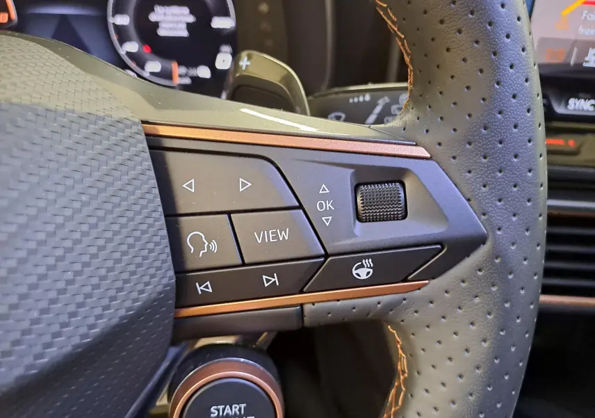 Gros plan sur les commandes du volant côté gauche en cuir perforé avec surpiqûres cuivrées du CUPRA Leon Noir Minuit 2025.