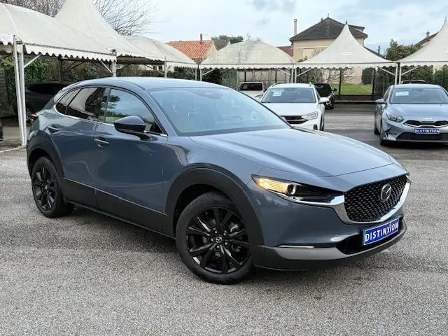 Vue 3/4 avant gauche d'un Mazda CX-30 2024 gris Polymetal avec jantes noires et calandre distinctive.