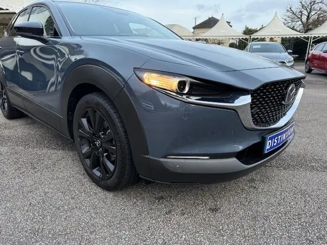 Vue 3/4 avant gauche d'un Mazda CX-30 2024 gris Polymetal avec phares allumés et jantes noires.