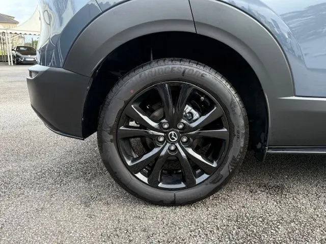 Gros plan sur la roue arrière gauche noire brillante du Mazda CX-30 2024 en Polymetal Grey.