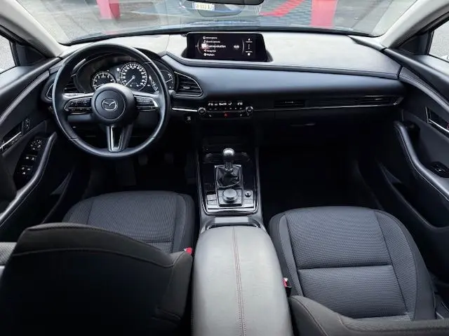Vue intérieure avant du Mazda CX-30 2024, tableau de bord noir avec écran central et levier de vitesse manuel.