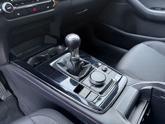 Gros plan sur la console centrale de la Mazda CX-30 2024, avec levier de vitesse manuel et finition noire brillante.