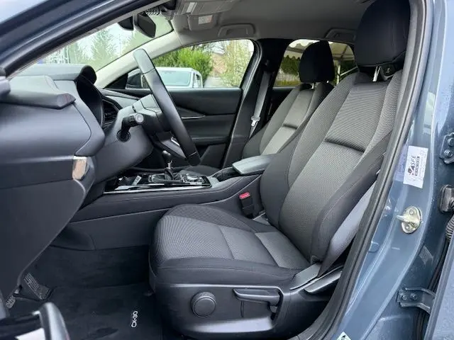 Vue intérieure côté conducteur de la Mazda CX-30 2024 Polymetal Grey, sièges tissu gris et tableau de bord moderne.