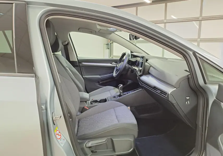 Vue intérieure côté conducteur de la Volkswagen Golf 1.5 TSI 2025 en Argent Dolomite, sièges tissu gris et tableau de bord moderne.