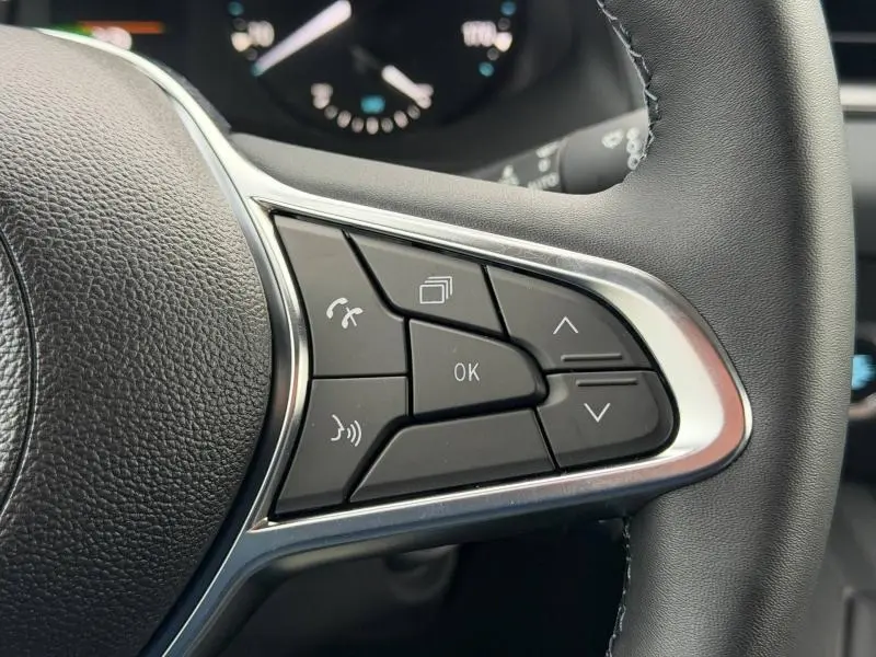 Gros plan sur les commandes multifonctions noires du volant cuir du Nissan Townstar blanc Minéral 2024.