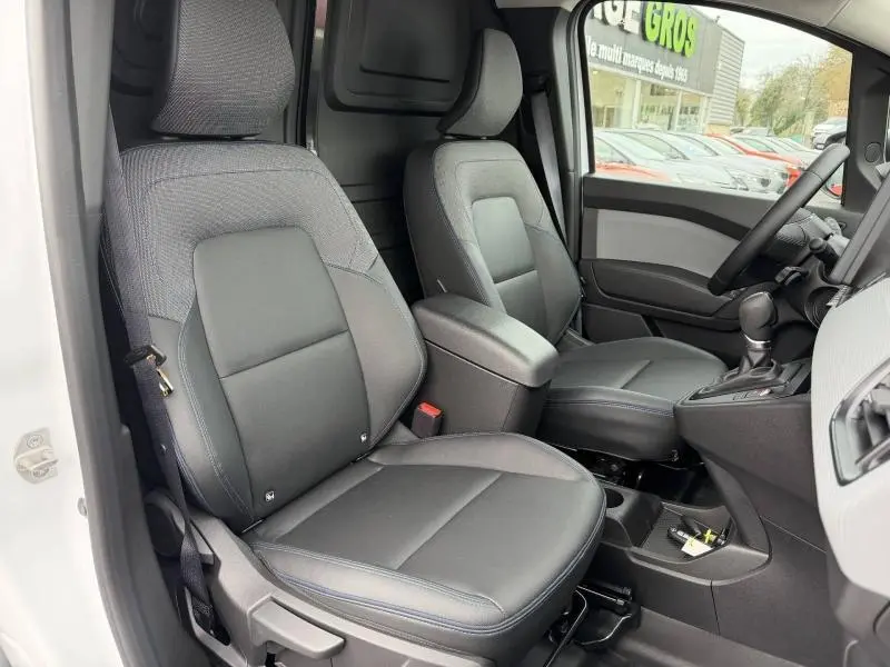 Vue intérieure côté conducteur du Nissan Townstar blanc minéral 2024, sièges noirs avec surpiqûres bleues et accoudoir central.