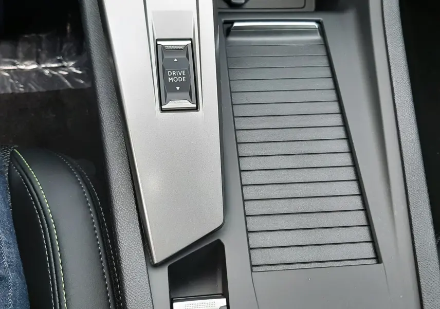 Vue rapprochée de la console centrale noire et grise avec bouton Drive Mode et frein à main électrique éclairé dans une Peugeot 308 hybride.