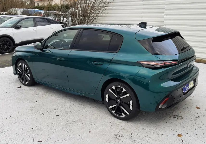 Peugeot 308 1.2 Hybrid GT bleu Lagoa vue 3/4 arrière droit, jantes noires et vitres teintées.