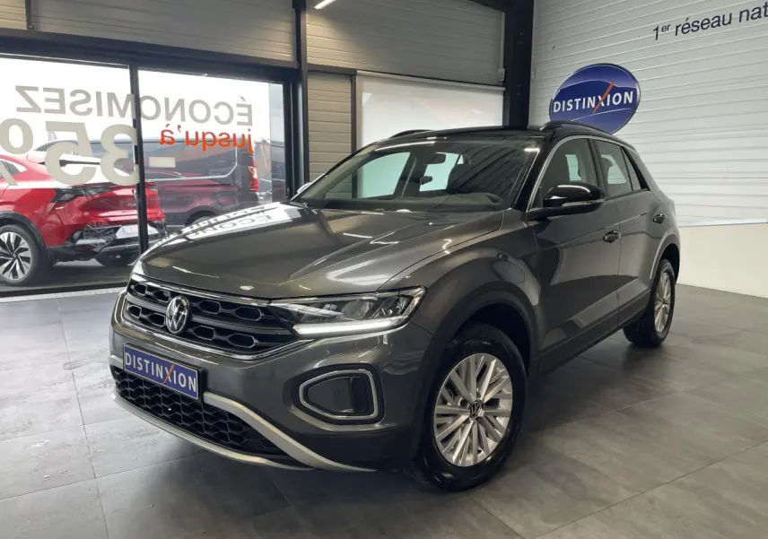 Volkswagen T-Roc 2025 gris Indium en 3/4 avant droit avec toit noir et jantes alliage 16 pouces dans un showroom.