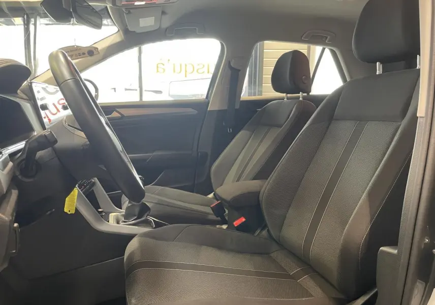 Vue intérieure côté gauche du Volkswagen T-Roc 2025 gris Indium, montrant les sièges avant en tissu noir et le volant multifonction.