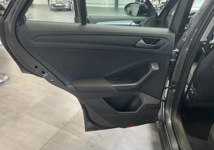 Vue intérieure de la porte arrière gauche du Volkswagen T-Roc Indium Gray 2025 avec garniture noire et poignée argentée.