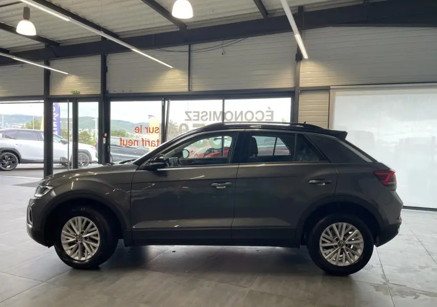 Volkswagen T-Roc 2025 gris Indium, vue de profil côté gauche en intérieur avec jantes alliage et toit noir.