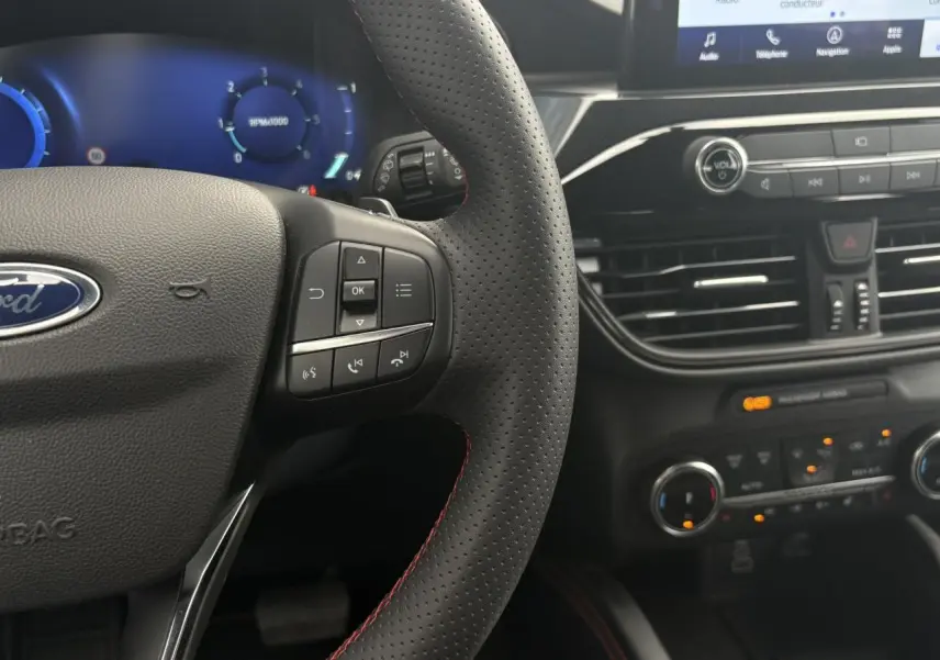Vue rapprochée du volant perforé noir avec surpiqûres rouges et tableau de bord numérique du Ford Kuga ST-Line 2023.