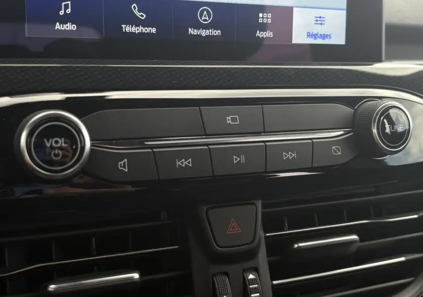 Gros plan sur la console centrale du Ford Kuga 2023, boutons audio et ventilation avec écran tactile en haut.