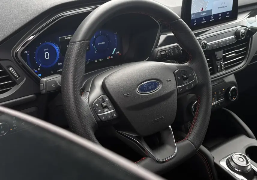 Vue rapprochée du volant cuir noir avec surpiqûres rouges et tableau de bord numérique du Ford Kuga 2023.