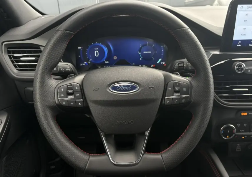 Vue rapprochée du volant noir perforé avec surpiqûres rouges du Ford Kuga 2023, tableau de bord numérique en arrière-plan.