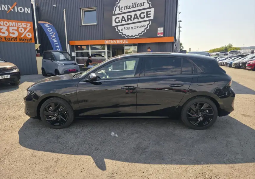 Opel Astra Hybrid 2024 noir profil côté gauche avec jantes alliage noires et vitres surteintées, stationnée devant un garage.