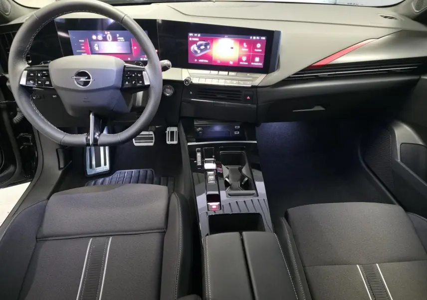 Intérieur avant de l’Opel Astra Hybrid 2024, vue du conducteur, tableau de bord noir avec écran tactile large et détails rouges.