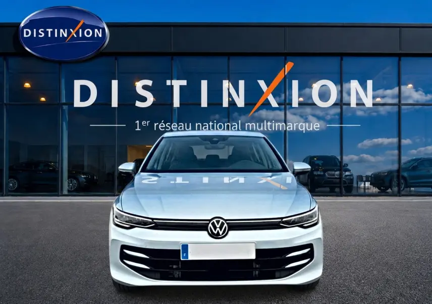 Vue avant d'une Volkswagen Golf 1.5 ETSI Evo2 bleu glacier garée devant une vitrine Distinxion.