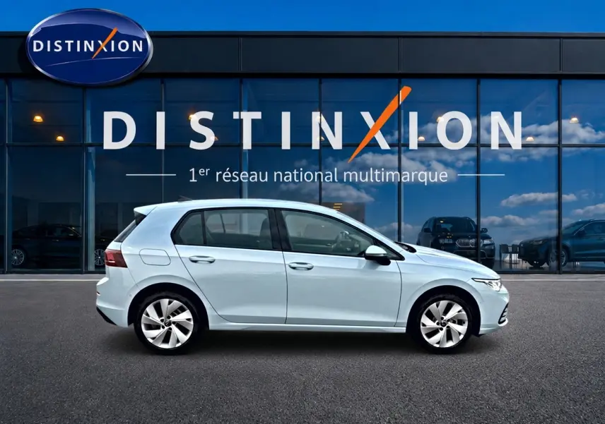 Volkswagen Golf 2026 bleu glacier vue de profil côté gauche devant une vitrine Distinxion.