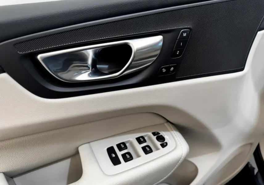Détail de la porte avant gauche intérieure beige du Volvo XC60 avec commandes de vitres et poignée chrome.
