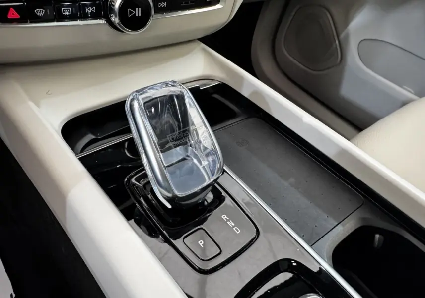 Gros plan sur la console centrale beige et noire du Volvo XC60 bleu, mettant en valeur le levier de vitesse automatique en cristal.