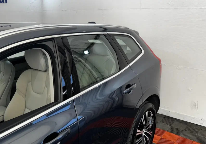 Vue latérale arrière droite d’un Volvo XC60 bleu avec sièges cuir clairs et jantes alliage noires.