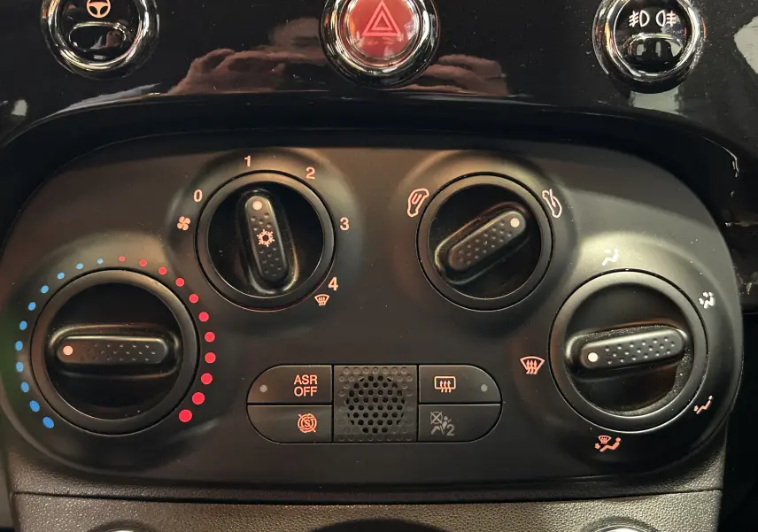 Gros plan sur les commandes de climatisation et sécurité du tableau de bord noir de la Fiat 500 2023 finition Pack Confort.