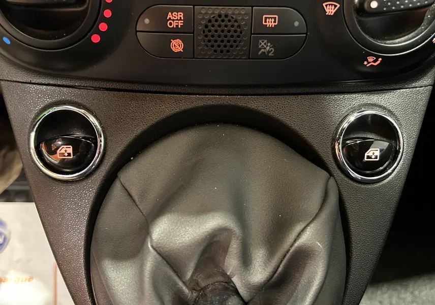 Gros plan sur la console centrale de la Fiat 500 noire 2023, mettant en valeur le levier de vitesse manuel et les commandes des vitres électriques.