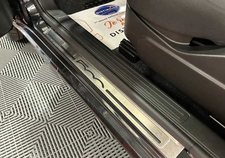 Gros plan sur la plaque de seuil de porte noire de la FIAT 500 2023 avec logo gravé et intérieur tissu sombre.