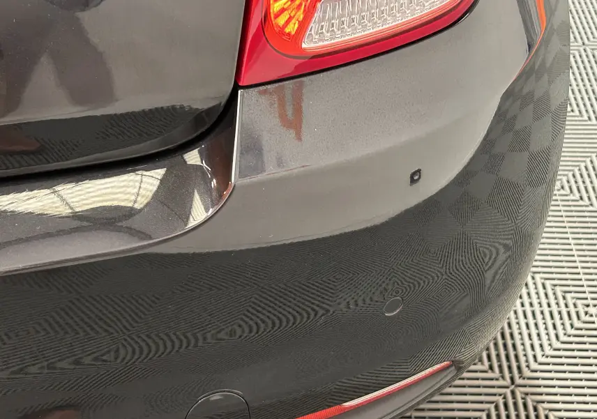 Gros plan sur le pare-chocs arrière noir d'une Fiat 500 2023, avec feu arrière et capteurs de radar de recul visibles.