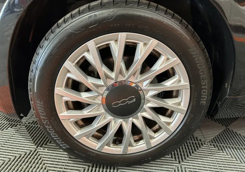Gros plan sur la roue avant droite noire d'une Fiat 500 2023 avec jante argentée au design étoilé.
