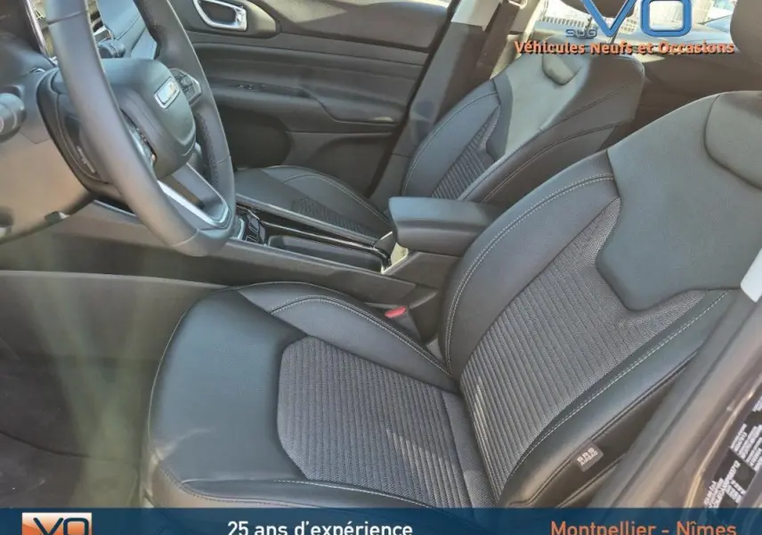 Intérieur avant du Jeep Compass gris 2024, sièges en cuir noir avec accoudoir central et volant visible côté conducteur.