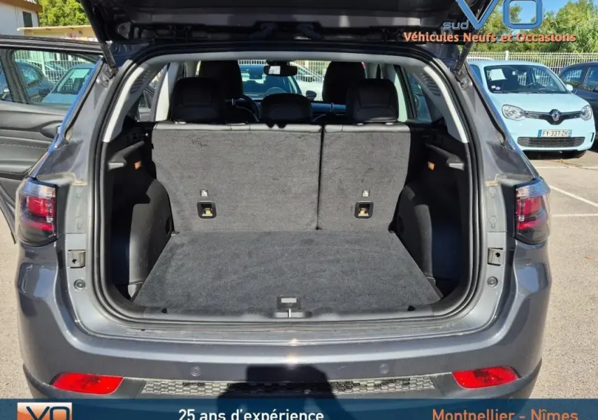 Coffre ouvert d'un Jeep Compass gris 3/4 arrière, montrant l'espace de chargement et les sièges arrière relevés.