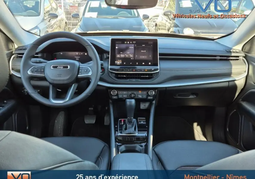 Intérieur du Jeep Compass 2024 en vue frontale, tableau de bord noir avec écran tactile central et volant multifonction.