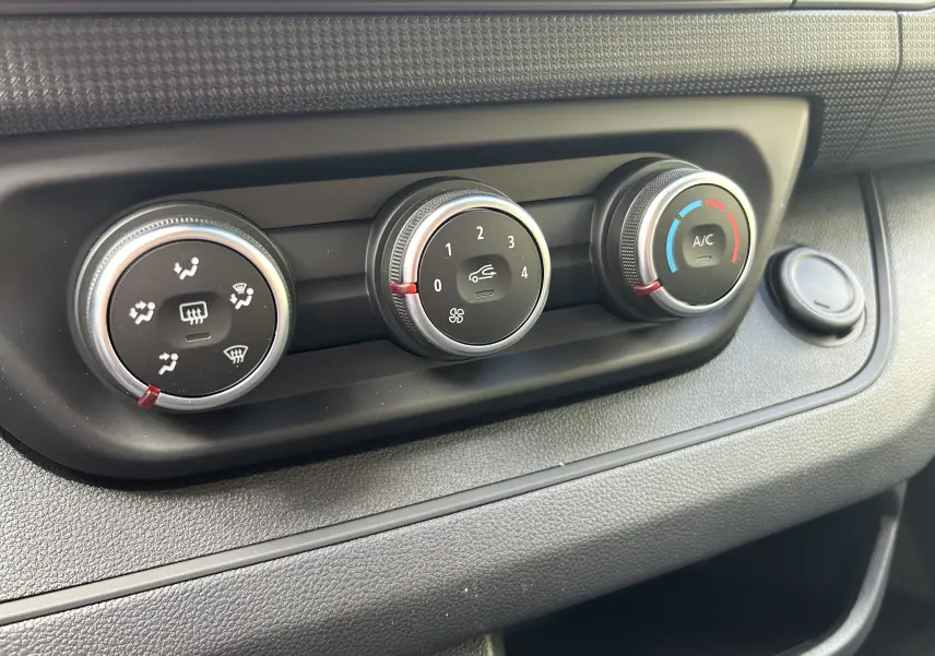 Gros plan sur les commandes de climatisation manuelle du Renault Trafic Combi blanc, avec réglages de ventilation et A/C.