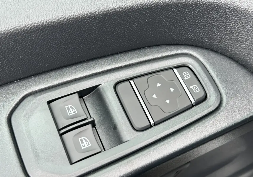 Gros plan sur les commandes de réglage des rétroviseurs et des vitres électriques côté conducteur du Renault Trafic Combi blanc.