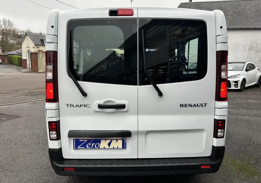 Vue arrière d’un Renault Trafic Combi blanc Glacier avec portes vitrées et essuie-glaces arrière visibles.