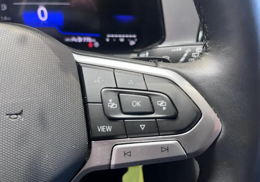 Gros plan sur les commandes multifonctions à gauche du volant cuir du Volkswagen T-Roc Deep Black Pearlescent 2025.