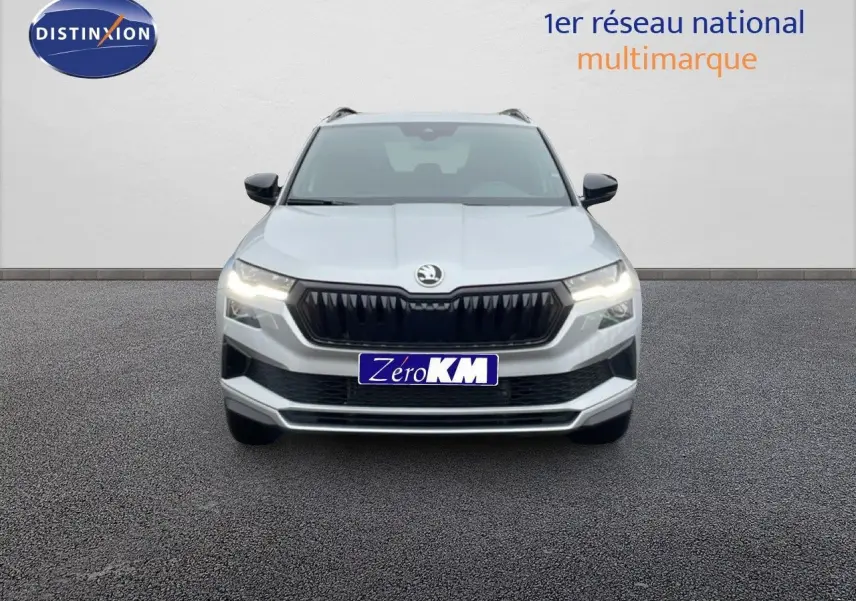 Vue frontale d’un Skoda Karoq gris argent métallisé avec calandre noire et phares allumés sur fond neutre.
