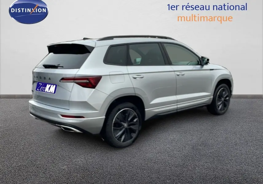 Vue 3/4 arrière droite d'un Skoda Karoq gris argent métal 2025 avec jantes noires et toit ouvrant.