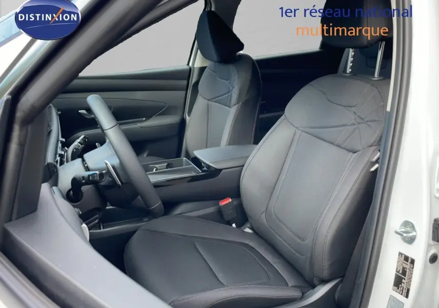 Vue intérieure côté conducteur du Hyundai Tucson 2026 blanc Atlas, sièges tissu noir et tableau de bord moderne.