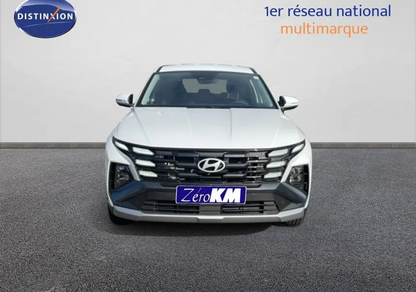 Vue frontale d’un Hyundai Tucson blanc Atlas 2026 avec calandre noire et feux LED distinctifs allumés.