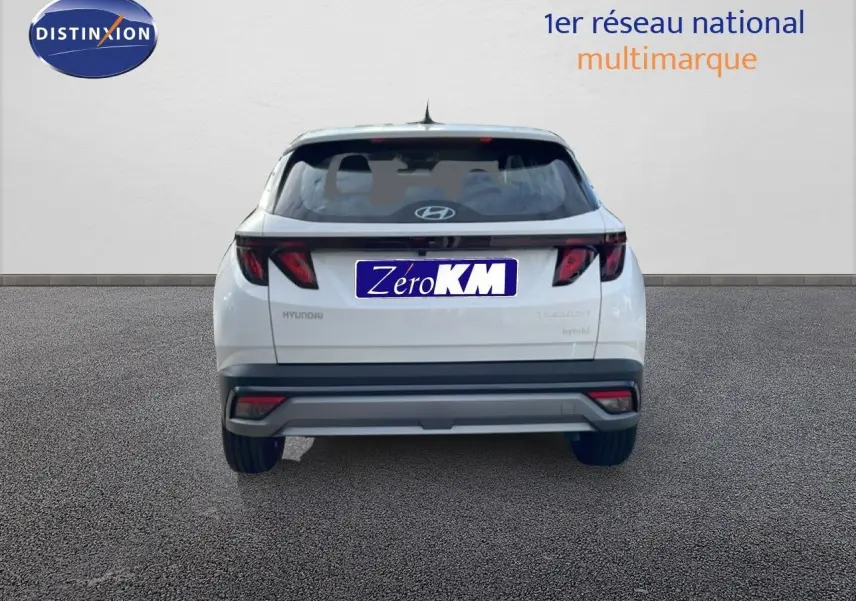 Vue arrière du Hyundai Tucson blanc Atlas 2026 hybride, avec feux arrière sombres et pare-chocs gris contrastant.