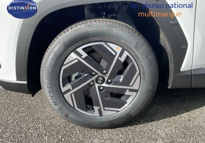 Gros plan sur la roue avant droite du Hyundai Tucson blanc Atlas, mettant en valeur la jante noire et grise au design géométrique.