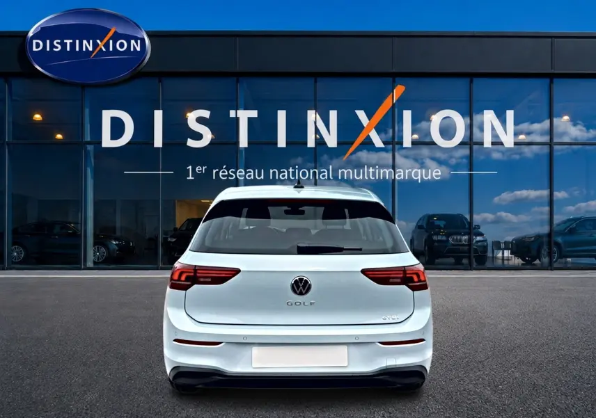 Vue arrière d'une Volkswagen Golf 1.5 etsi evo2 116 life dsg7 bleu glacier, garée devant une vitrine Distinxion.