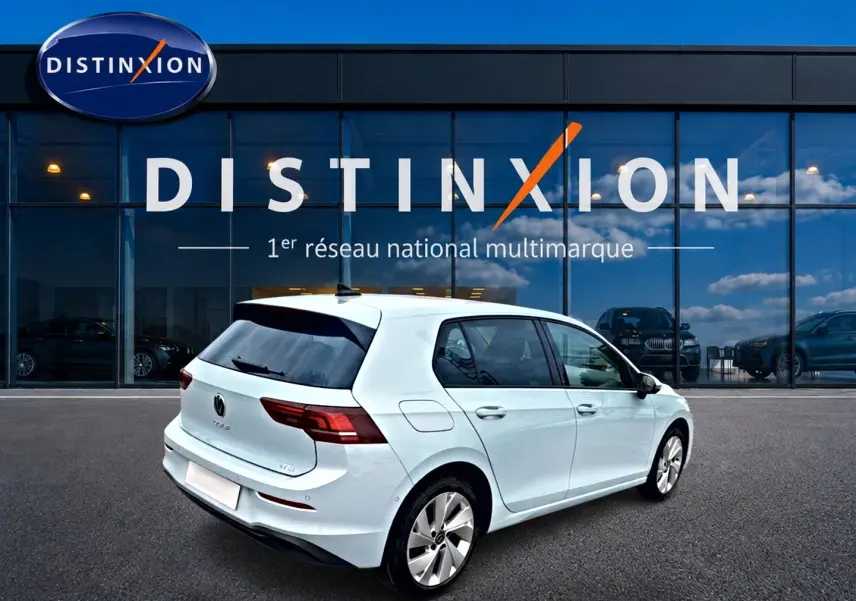 Vue 3/4 arrière droite d'une Volkswagen Golf blanche garée devant une vitrine avec logo Distinxion.