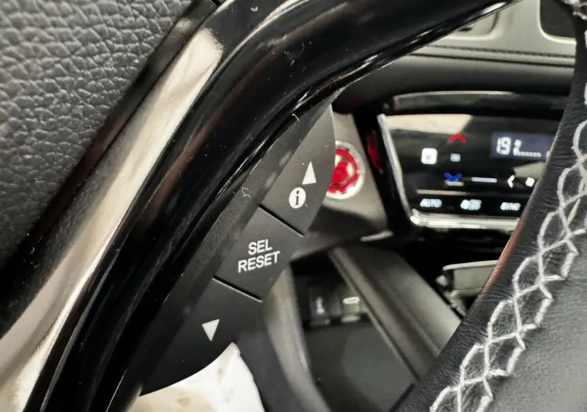 Gros plan sur le volant cuir noir avec surpiqûres blanches du Honda HR-V 1.5 i-VTEC 130, tableau de bord digital en arrière-plan.